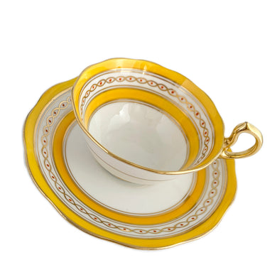 This antique bone china footed teacup and saucer is so sweet! Both the cup and saucer have a lovely scalloped edge, hand painted gold gilt bands over yellow and white glazed porcelain and a gold gilt infinity ribbon dotted in orange. Produced by Royal Albert Crown China, England. Based on the maker's mark, dates to 1927 - 1935.  In excellent condition, free from chips, cracks or repairs. Maker's mark on the bottom of both pieces. Teacup is marked with the number 591. 