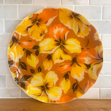 This retro FAB serving tray screams SPRING with its vibrant orange and yellow hibiscus flowers with brown and white accents on an ochre ground. This gorgeous decorator fabric was pressed between 2 layers of a plastic material and molded into a tray with a sweet ruffled edge. Produced by Hardy Glenwood in Canada, circa 1960s/70s. A great addition to your spring and summer entertaining!

In excellent condition.

Measures 13 inches