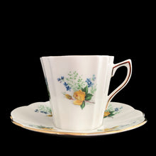 Load image into Gallery viewer, A lovely vintage white bone china scalloped shaped teacup and saucer featuring yellow roses and blue flowers. Crafted by Montrose, England, circa 1970s. The perfect vessel for an excellent cuppa tea!

In excellent condition, no chips, cracks or repairs. Maker&#39;s marks on the bottom.

Teacup measures 3 x 2 7/8 inches | Saucer measures 5 1/2 inches
