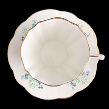 Load image into Gallery viewer, A lovely vintage white bone china scalloped shaped teacup and saucer featuring yellow roses and blue flowers. Crafted by Montrose, England, circa 1970s. The perfect vessel for an excellent cuppa tea!

In excellent condition, no chips, cracks or repairs. Maker&#39;s marks on the bottom.

Teacup measures 3 x 2 7/8 inches | Saucer measures 5 1/2 inches
