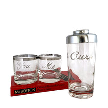 Load image into Gallery viewer, This mid-century vintage cocktail set features two silver-rimmed glasses labeled You and Me in elegant silver script, accompanied by a matching cocktail shaker marked Ours with a chrome lid. Crafted by Queens Lustreware, USA, 1950s. This set makes an ideal gift for weddings or housewarmings, celebrating togetherness with timeless style.

All pieces are in excellent vintage condition.

Shaker measures 2 3/4 x 6 inches. Capacity 12 ounces.

Glasses measure 2 1/2 x 2 3/4 inches. Capacity 4 ounces.
