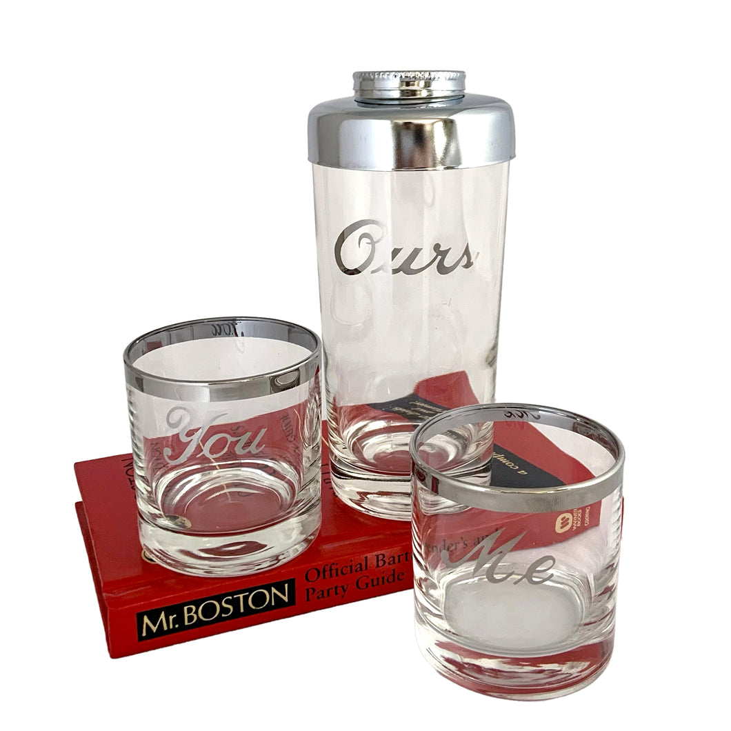 This mid-century vintage cocktail set features two silver-rimmed glasses labeled You and Me in elegant silver script, accompanied by a matching cocktail shaker marked Ours with a chrome lid. Crafted by Queens Lustreware, USA, 1950s. This set makes an ideal gift for weddings or housewarmings, celebrating togetherness with timeless style.

All pieces are in excellent vintage condition.

Shaker measures 2 3/4 x 6 inches. Capacity 12 ounces.

Glasses measure 2 1/2 x 2 3/4 inches. Capacity 4 ounces.