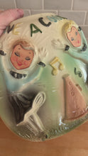 Load and play video in Gallery viewer, Movie of rare vintage ceramic corner cookie jar features brunette and blonde cheerleaders in old-fashioned outfits, cheering underneath the words Have A Cookie in between is a megaphone on the grass that reads cookie time all glazed in shades of green, blue, yellow brown and black on a cream ground, topped with a rust-brown megaphone on the lid. The piece-de-resistance are the cheerleaders holographic facial expressions that change from eyes open with a wide smile to eyes shut with closed smiles. 
