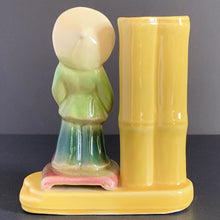 Load image into Gallery viewer, Sweet decorative yellow vase with an Asian figure on a podium standing beside a bamboo stalk which acts as the vase. Shape 702, produced by Shawnee Pottery USA. Perfect as a bud vase or your favourite mini plant or succulent.  In good vintage condition, no cracks. Small glaze loss spot to front of the yellow foot, see photos.  Measures 5 x 2 1/2 x 5 1/2 inches
