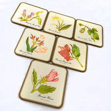 Load image into Gallery viewer, A vintage set of six square round edged coasters, each decorated with an illustration of a tropical flower on an off-white background, bordered in gold with cork-backing. Coasters make the perfect resting place for drinking glasses or mugs to protect your furniture from being marked. Made by Pimpernel in England. Makes a great housewarming or hostess gift!  In excellent vintage condition.  Each coaster measures 4-1/8&quot; x 4-1/8&quot;
