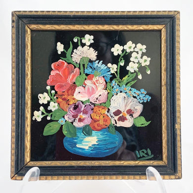 A signed still life oil painting on glass. This piece depicts a blue vase filled with pansies, roses and white flowers back painted in black. It is signed by the artist in the lower right corner with 