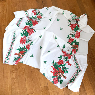 This festive vintage white cotton Christmas themed tablecloth is decorated with red and white poinsettia flowers, green holly leaves, bows and candles. A lovely table covering for the holiday season! In excellent condition, free from stains/tears.  Measures 58