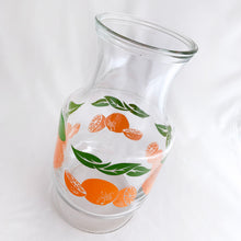 Load image into Gallery viewer, Bring a little sunshine to table with this retro glass carafe decorated with vibrant oranges and white flowers. Produced by Anchor Hocking Glass Company USA. Production began on this pattern in 1950s. This piece was manufactured in 1987. This carafe or pitcher is perfect for juice, iced tea, lemonade, water or mix up some cocktails!  In excellent condition, no chips or cracks and the colour is vibrant orange and green.  Measures 4 x 8 5/8 inches
