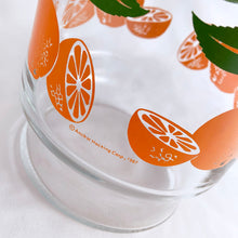 Load image into Gallery viewer, Bring a little sunshine to table with this retro glass carafe decorated with vibrant oranges and white flowers. Produced by Anchor Hocking Glass Company USA. Production began on this pattern in 1950s. This piece was manufactured in 1987. This carafe or pitcher is perfect for juice, iced tea, lemonade, water or mix up some cocktails!  In excellent condition, no chips or cracks and the colour is vibrant orange and green.  Measures 4 x 8 5/8 inches
