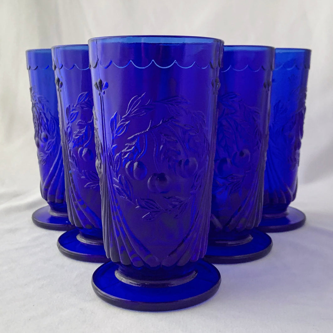 RARE FIND! Charming vintage cobalt blue Cherry 7-15 iced tea footed glass tumblers. Produced by the LG Wright Glass Company, USA, circa 1960s. The pattern consists of a trio of cherries surrounded by a wreath pf leaves bordered by a fluted design and a scalloped detail below the rim. In great vintage condition. One glass has a manufacturer's defect at the base, one glass has minor flea bites at the rim. The others are in excellent condition, free from chips/cracks.