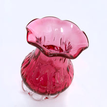 Load image into Gallery viewer, Beautiful, heavy-weighted cranberry glass vase with clear scalloped foot. The vase has an urn-shape with a ribbed detail and ruffled edge. A very nice piece of glass to use for a floral bouquet or repurpose to fold make-up brushes or q-tips. We see a lot of these pieces attributed to Pilgrim Glass, but without a maker&#39;s mark we can&#39;t be certain.  In excellent condition, free from chips/cracks/repairs.  Measures 2 7/8 x 4 inches

