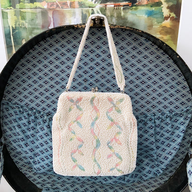Unique handmade vintage mid-century era evening bag adorned in cream glass seed beads and ribbons of multi-colour pastel embroidery, topped with a matching beaded strap and silver toned metal kiss closure. The interior is lined with cream satin with open pocket. The bag is large enough for a cell phone, credit cards/cash, compact/lipstick. Produced in Japan. An absolutely stunning piece that would make an incredible bridal accessory!
Excellent used vintage condition.