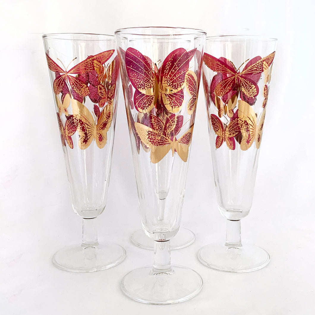 Sip a cold beer or bubbly champagne in style with these stunning vintage pilsner glasses decorated with bright gold and deep pink butterflies. Maker unknown. Circa 1960s.  In excellent condition, free from chips/cracks/wear.  Measures 8.5