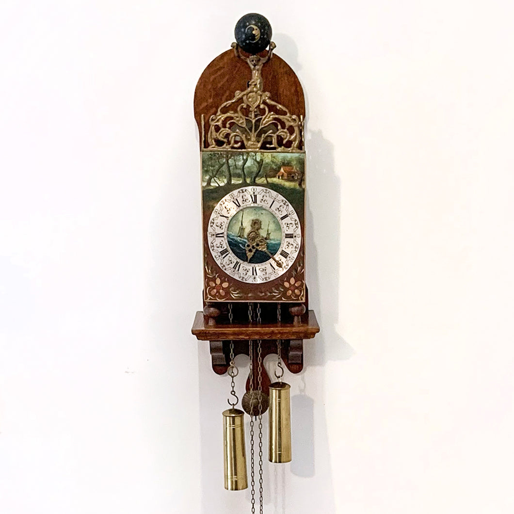 Vintage folklore wood wall clock with brass scrollwork, brass Atlas holding a black globe above its head, decorated with the moon and stars. The clock dial has with roman numerals, numbers and decorative elements in black with central hand painted scene of the sea with two sailing ships, above the dial is a pastoral scene and below folk art florals. Eight day movement with chime striking on the hour and every half hour. Brass weights, pendulum and chains included. Warmink WUBA, Netherlands, circa 1960s.