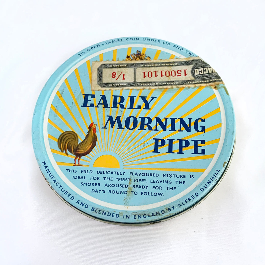 Vintage Early Morning Pipe tobacco tin with original interior wrap and tariff sticker. The lid has a great graphic of a sunrise and a rooster crowing on a pale blue background. Produced by Dunhill in England. In good vintage condition with minor wear.  Dimensions: 4