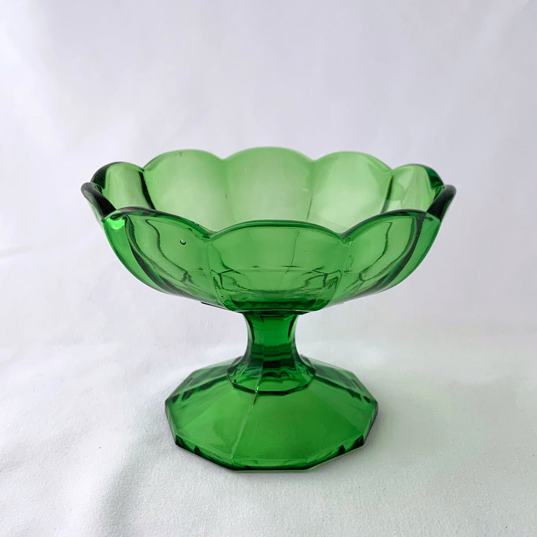 A vibrant emerald green footed compote or candy bowl. It has a beautiful scalloped both atop a 10-sided footed pedestal. Perfect to serve candies or nuts. Easily repurpose as a catchall or vanity/dresser to hold cotton balls, bath bombs or trinkets. It's such an elegant statement piece and will and drama to any home decor style!  In excellent condition, no chips or cracks. Maker unknown.  Measures 5 3/8 x 3 7/8 inches