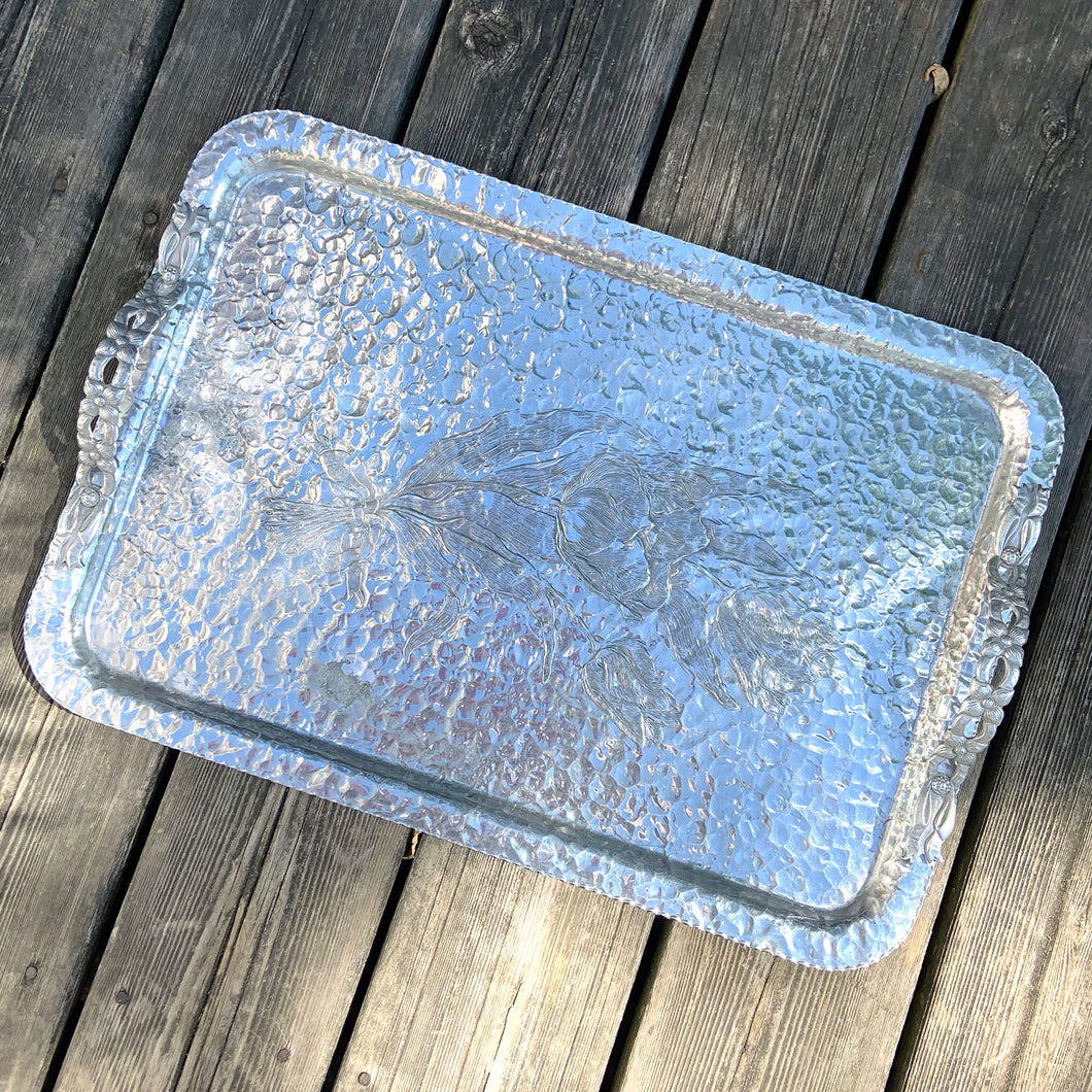 One of the pretties pieces of hammered aluminum we've encountered! This sweet serving tray has decorative ribbon style handles detailed with floral details and embossed tulips on the tray surface (shape 408). Made by Rodney Kent, circa 1950. A great addition to your serveware or bar cart.  In excellent condition. Manufacturer's marks on the bottom.  Measures 20 x 14