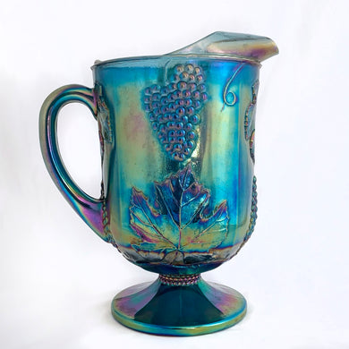 Gorgeous vintage iridescent blue Harvest grapes and leaves carnival glass pitcher Crafted by Colony (Indiana) Glass Co., USA, 1973 - 1976. This pitcher would look amazing on any tablescape or use it to create a beautiful floral display.


In excellent condition, no chips or cracks.

Measures 6 x 10 inches

Capacity 64 ounces
