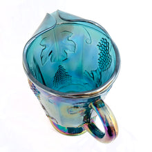 Load image into Gallery viewer, The words &quot;stunning&quot; and &quot;elegant&quot; embody this incredible blue carnival glass pitcher in the &quot;Harvest&quot; pattern of grapes and leaves. Made by Colony (Indiana) Glass Co. between 1973 - 1976. This pitcher would look amazing on any tablescape or use it for a beautiful floral bouquet.  In excellent condition, no chips or cracks.  Measures 6&quot; x 10&quot;, holds 64oz
