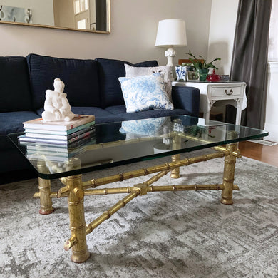 Stunning authentic Hollywood Regency faux bamboo coffee table. The table features a sturdy wood frame with half inch thick glass top. The base has a unique decorative finish which lends itself to either a glam or boho decor style. Its petite size makes it the perfect choice for a small space while adding incredible impact. The table base in excellent vintage condition with minor wear and the one inch thick glass top is free from chips. Measures 42 x 24 x 16-1/2 inches