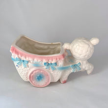 Load image into Gallery viewer, kitsch adorable vintage mid-century ceramic planter of a sweet little lamb pulling a baby carriage pram with ribbons and flowers in pink and blue on a white. It’s perfect for a tiny houseplant/succulent or repurpose to hold for baby lotions/accessories, pens or make-up brushes. Easter gift fill with chocolate eggs. Made by Inarco in Japan, shape E5432. Good vintage condition, no chips/cracks/repairs, some glaze loss on one ear (see photos). Measures 6 3/4 x 3 x  3 3/4 inches
