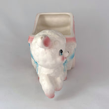 Load image into Gallery viewer, kitsch adorable vintage mid-century ceramic planter of a sweet little lamb pulling a baby carriage pram with ribbons and flowers in pink and blue on a white. It’s perfect for a tiny houseplant/succulent or repurpose to hold for baby lotions/accessories, pens or make-up brushes. Easter gift fill with chocolate eggs. Made by Inarco in Japan, shape E5432. Good vintage condition, no chips/cracks/repairs, some glaze loss on one ear (see photos). Measures 6 3/4 x 3 x  3 3/4 inches
