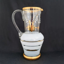 Load image into Gallery viewer, Vintage blown glass pitcher beautifully detailed with white Lily-of-the-Valley with gold leaves along with soft white and gold bands and applied blown glass handle. The perfect piece of serveware for spring and summer gatherings! Produced in Romania, circa 1950s.  In excellent condition, free from chips/cracks/wear.  Measures 5 x 11 1/8 inches
