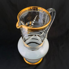 Load image into Gallery viewer, Vintage blown glass pitcher beautifully detailed with white Lily-of-the-Valley with gold leaves along with soft white and gold bands and applied blown glass handle. The perfect piece of serveware for spring and summer gatherings! Produced in Romania, circa 1950s.  In excellent condition, free from chips/cracks/wear.  Measures 5 x 11 1/8 inches
