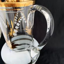 Load image into Gallery viewer, Vintage blown glass pitcher beautifully detailed with white Lily-of-the-Valley with gold leaves along with soft white and gold bands and applied blown glass handle. The perfect piece of serveware for spring and summer gatherings! Produced in Romania, circa 1950s.  In excellent condition, free from chips/cracks/wear.  Measures 5 x 11 1/8 inches
