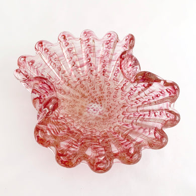 A stunning vintage pink and clear art glass shell shaped ashtray. This mid century piece has thick, ribbed glass in the style of a sea shell with controlled bubbles or bullicante and liberally infused with gold aventurine flecks. The wide scalloped edges are hand tooled. Attributed to Barovier and Toso, Murano, Italy, circa 1960. In good vintage condition. Polished bottom with minor bites which do not detract from the beauty of this piece.  Size: 8-1/4 x 6-1/4 x 2-3/4