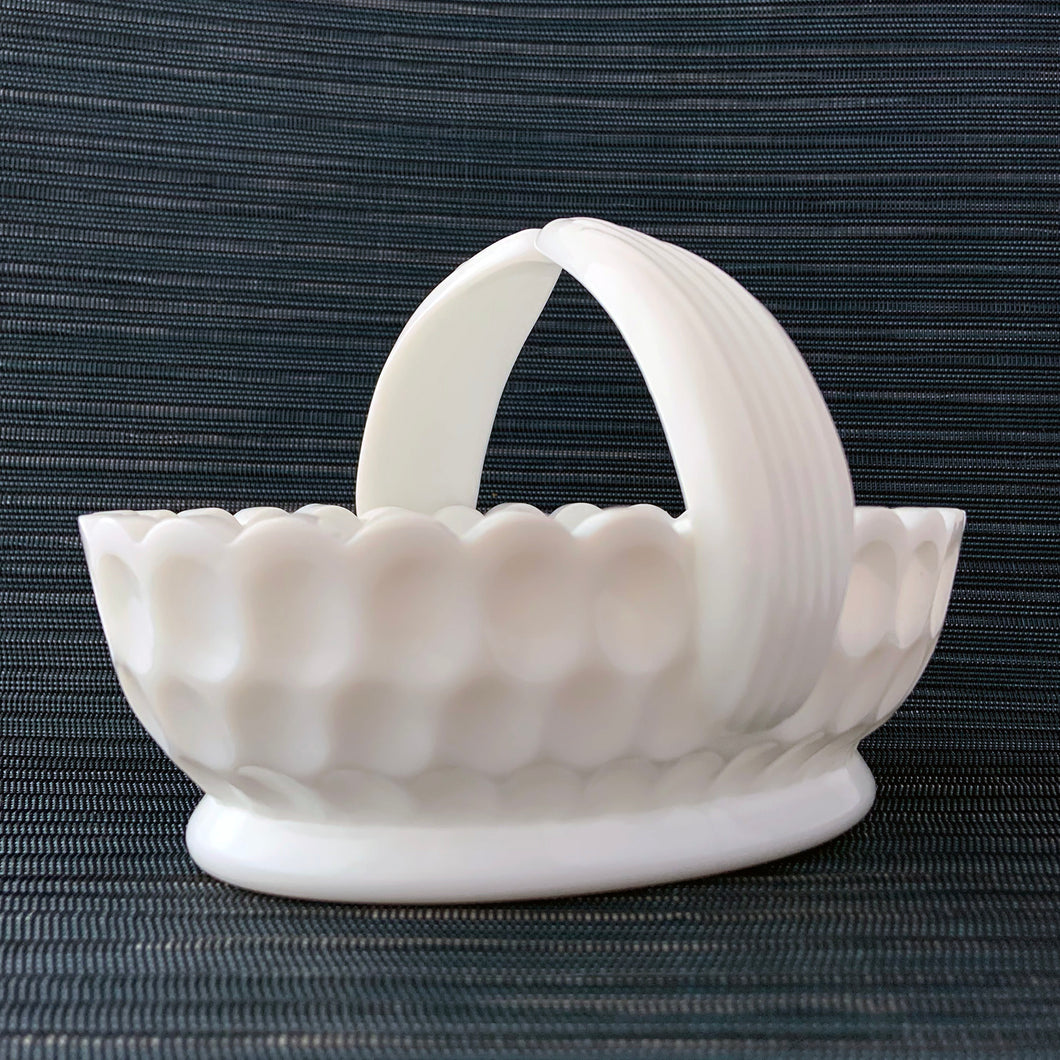 Vintage oval shaped milk glass thumbprint patterned basket with scalloped edge and split handle with ribbed detail. A pretty piece to use for trinkets, candy or as a serving dish. Produced by the Fenton Glass Company as part of their the Olde Virginia Glass line, circa 1970s.  In excellent condition, free from chips/cracks.  Measures 6 1/2 x 4 1/2 x 5 inches