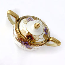 Load image into Gallery viewer, Elegant and beautifully hand painted antique porcelain oval-shaped creamer and covered sugar bowl with clematis flowers in shades of purple and gold vines with gold moriage details. The base of each piece show the Noritake stamp called the Maruki mark which was produced between 1906 to 1925. The sugar bowl is in excellent condition free from chips, cracks or repairs and has minor wear to the gold band on the lid, see photos. The creamer has a vertical crack on the body near the handle.
