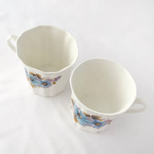 Load image into Gallery viewer, Treat yourself to a cuppa in this lovely feminine shaped fine bone china mug featuring blue and purple flowers with green leaves on white bone china. Crafted by Royal Grafton, England, circa 1970s. Grafton made these mugs with many floral designs — collect them all!  In excellent condition, no chips, cracks or crazing. Marked on the bottom with &quot;Royal Grafton, Fine Bone China, Made in England&quot;.  Measures 3 1/4 x 3 1/4 inches
