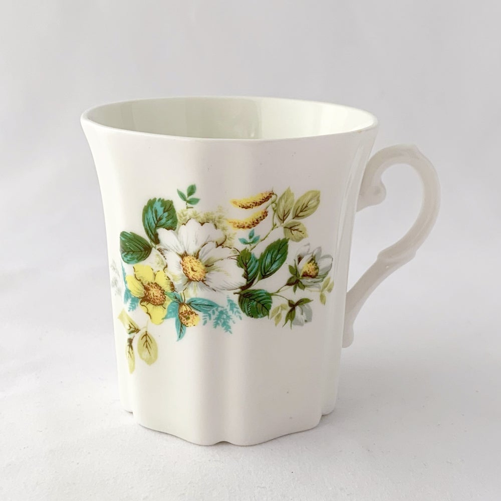 Treat yourself to a cuppa in this lovely feminine shaped fine bone china mug featuring beautiful white and yellow flowers with green leaves on white bone china. Crafted by Royal Grafton, England, circa 1970s. Grafton made these mugs with many floral designs — collect them all!  In excellent condition, no chips, cracks or crazing. Marked on the bottom with 
