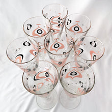 Load image into Gallery viewer, Rare. Highly collectible vintage mid-century atomic style Seville pilsner champagne glasses. Graphic geometric design in swirls of pink, black and gold. Original wood handled brass caddy. Produced by the Libbey Glass Company, circa 1960. In very good vintage condition with some wear to the gold rim, free chips. Each glass measures approximately three by eight inches.

