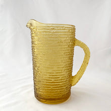 Load image into Gallery viewer, Enjoy freshly made beverages with this vintage &quot;Soreno Gold&quot; pressed glass pitcher. Made with a textured bark pattern and a luminous gold colour, it&#39;s perfect for serving juice, lemonade, or ice tea. Produced by Anchor Hocking Glass Company, USA between 1966-1970.  In excellent condition - free from chips or cracks.  Measures 4 x 7 inches  Capacity of 1 litre or quart
