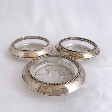 Gorgeous set of three vintage sterling silver rimmed cut crystal coasters. The smooth silver rim features a beaded inner edge and the crystal is cut in a starburst pattern. Elegant and perfect to protect your furniture from condensation marks! Produced by Frank M. Whiting, circa early 20th century, pre-1926.  In good vintage condition with general wear from normal age and use. Marked 