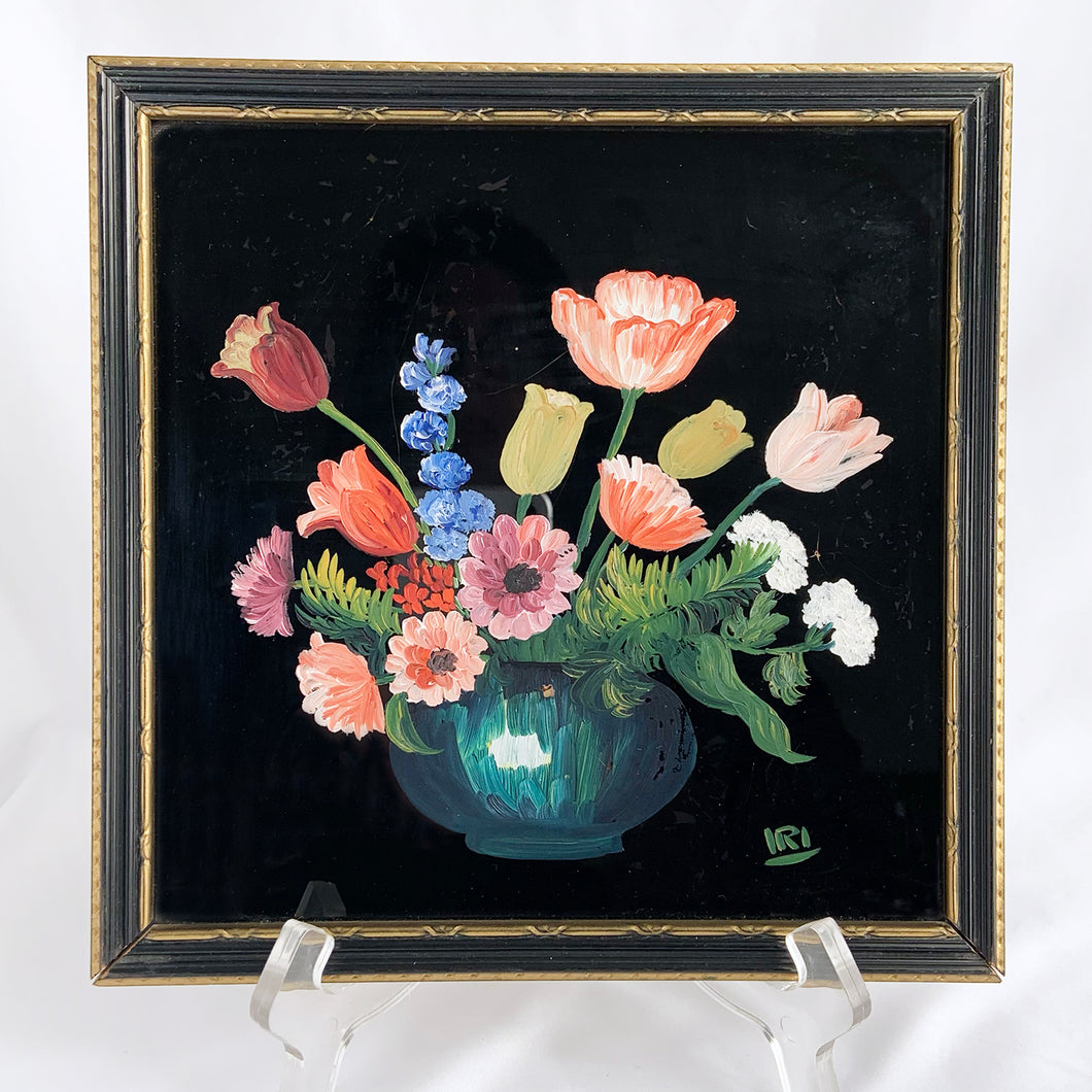 A signed still life oil painting on glass. This piece depicts a blue vase filled with red tulips and anemones, blue delphiniums and white candy tuft flowers back painted in black. It is signed by the artist in the lower right corner with 