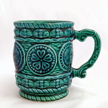 Load image into Gallery viewer, Lovely glazed ceramic teal coloured mug with raised floral medallions, rope details and a sculpted handle. Produced by Noritake for Gift Craft, circa 1950. Use as intended or repurpose as a decorative pencil or make-up brush holder.  In excellent vintage condition, free from chips/cracks.
