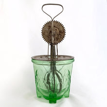 Load image into Gallery viewer, Antique vintage green uranium/vaseline depression era glass footed 2 cup hand beater mixer. The glass cup glows beautifully under black light, has an artichoke design on all 4 sides, measuring lines in 1/4 cup increments and four square feet. Bottom is marked &quot;Patent Applied For&quot;. Produced by Hazel-Atlas Glass, circa 1920.  In overall excellent condition, free from chips/cracks. The metal beater has wear commensurate with age and works well.  Glass measures 4-1/2&quot; x 4-1/4&quot;. Total height with beater is 10&quot;
