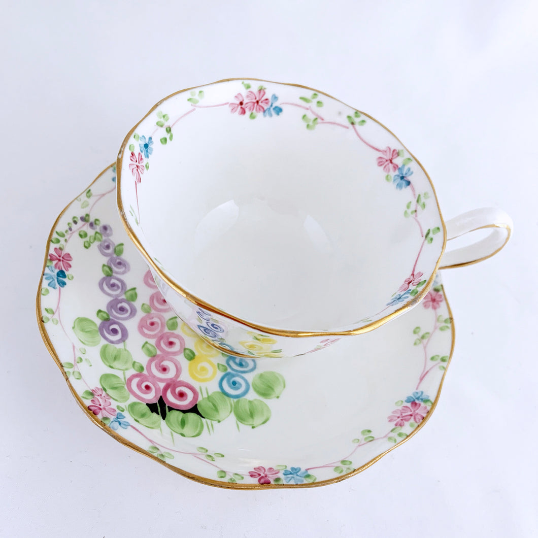 Antique bone china footed teacup and saucer with scalloped edge, hand painted whimsical pastel coloured foxglove florals and rimmed with gold gilt. Produced by Royal Albert, England, circa 1917 - 1927. In excellent condition, free from chips, cracks and repairs. Pattern number 2475 and maker's marks are on the bottom of the teacup and maker's mark on the saucer. Teacup measures 3-3/4