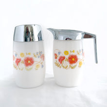 Load image into Gallery viewer, Classic vintage set of white milk glass creamer pitcher and sugar dispenser, both decorated with a spray of red poppies, yellow daisies and bluebells. The creamer has a chrome collar/handle and the sugar dispenser has a chrome flip top lid.  Produced by Dominion Glass Canada, circa 1970.  In excellent condition with only minor wear to the chrome, the glass is free from chips/cracks.  Creamer measures 2-3/4&quot; x 5&quot;  Sugar dispenser measures 2-3/4&quot; x 5-1/2&quot;
