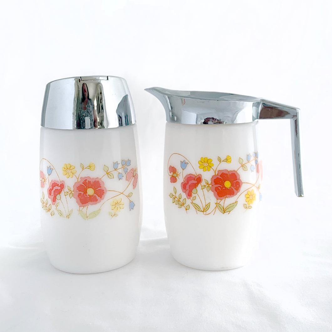 Classic vintage set of white milk glass creamer pitcher and sugar dispenser, both decorated with a spray of red poppies, yellow daisies and bluebells. The creamer has a chrome collar/handle and the sugar dispenser has a chrome flip top lid.  Produced by Dominion Glass Canada, circa 1970.  In excellent condition with only minor wear to the chrome, the glass is free from chips/cracks.  Creamer measures 2-3/4