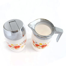 Load image into Gallery viewer, Classic vintage set of white milk glass creamer pitcher and sugar dispenser, both decorated with a spray of red poppies, yellow daisies and bluebells. The creamer has a chrome collar/handle and the sugar dispenser has a chrome flip top lid.  Produced by Dominion Glass Canada, circa 1970.  In excellent condition with only minor wear to the chrome, the glass is free from chips/cracks.  Creamer measures 2-3/4&quot; x 5&quot;  Sugar dispenser measures 2-3/4&quot; x 5-1/2&quot;
