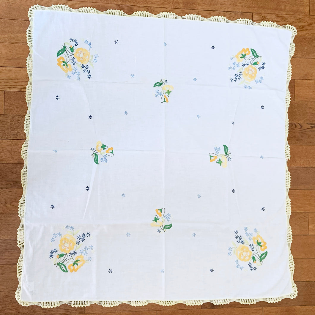 Vintage crewel embroidered tablecloth with flowers in sunny shades of yellow and blue with green accents and edged in a crocheted border.  In good vintage condition with one small repair.  Measures 41 x 41 inches