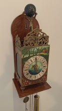 Load and play video in Gallery viewer, Vintage folklore wood wall clock with brass scrollwork, brass Atlas holding a black globe above its head, decorated with the moon and stars. The clock dial has with roman numerals, numbers and decorative elements in black with central hand painted scene of the sea with two sailing ships, above the dial is a pastoral scene and below folk art florals. Eight day movement with chime striking on the hour and every half hour. Brass weights, pendulum and chains included. Warmink WUBA, Netherlands, circa 1960s.
