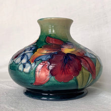 Load image into Gallery viewer, Gorgeous vintage mid-century hand painted squat flower vase in the &quot;Orchid&quot; pattern on green ground, hand painted in shades of red, yellow, purple and blue using the slip glaze technique. Made by Moorcroft Pottery in Stoke-on-Trent, England, circa 1950.  In excellent condition, no chips, cracks or repairs, crazing present. Initials of Walter Moorcroft in blue, impressed marks &quot;MOORCROFT&quot; and &quot;MADE IN ENGLAND&quot;.  Measures 3-1/4&quot; high
