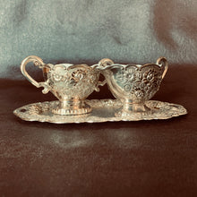 Load image into Gallery viewer, This creamer and sugar set has the prettiest floral details and a smooth white enamel interior with matching tray. Add some shine to your table scape!  In excellent condition.
