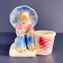 Load image into Gallery viewer, Imagine this older Asian gentleman protecting himself with his umbrella while he sells his wares at the market. Produced by Shawnee Pottery, USA, circa 1940s. Perfect for your favourite mini plant or succulent.  A wonderfully detailed vintage ceramic planter glazed in subtle shades of beige, blue and red.  In excellent condition, free from chips/cracks.  Measures 5 x 3 1/4 x 5 1/4 inches
