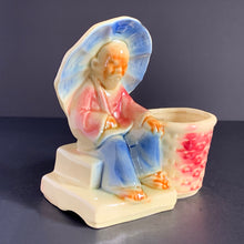 Load image into Gallery viewer, Imagine this older Asian gentleman protecting himself with his umbrella while he sells his wares at the market. Produced by Shawnee Pottery, USA, circa 1940s. Perfect for your favourite mini plant or succulent.  A wonderfully detailed vintage ceramic planter glazed in subtle shades of beige, blue and red.  In excellent condition, free from chips/cracks.  Measures 5 x 3 1/4 x 5 1/4 inches
